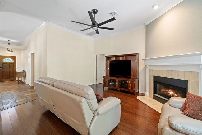 Living area featuring ceiling fan, ornamental molding, a tile fireplace, and wood finished floors | Image 11