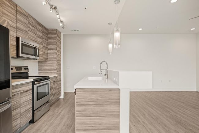 Kitchen with modern cabinets, appliances with stainless steel finishes, light wood finished floors, light countertops, and recessed lighting | Image 8