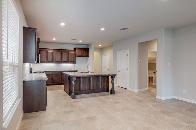 Kitchen featuring a kitchen island with sink, a sink, tasteful backsplash, light stone counters, and baseboards | Image 6