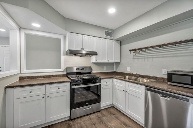 Kitchen featuring stainless steel appliances, a sink, under cabinet range hood, dark countertops, and white cabinetry | Image 6