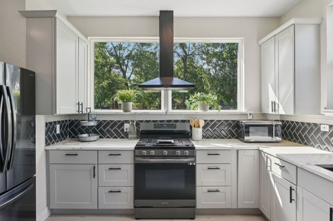 Kitchen with stainless steel range with gas cooktop, freestanding refrigerator, tasteful backsplash, island range hood, and light stone countertops | Image 11