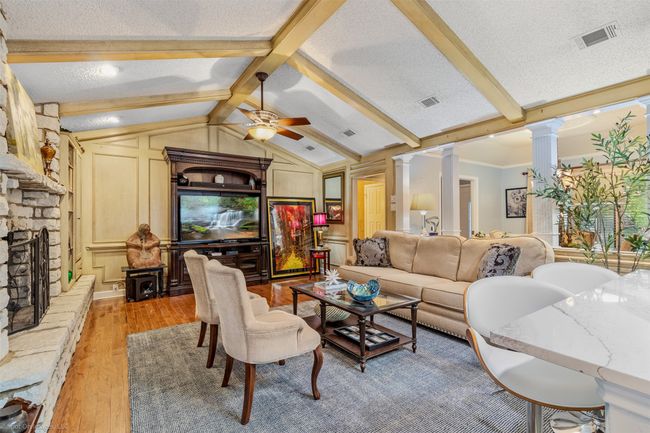 Large living area is conveniently connected with the kitchen and breakfast areas and features, hardwood flooring, a cathedral style ceiling, wood beam accents, a decorative stone fireplace | Image 9