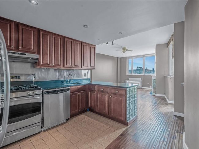 Kitchen featuring stainless steel appliances, under cabinet range hood, a ceiling fan, a peninsula, and dark countertops | Image 4