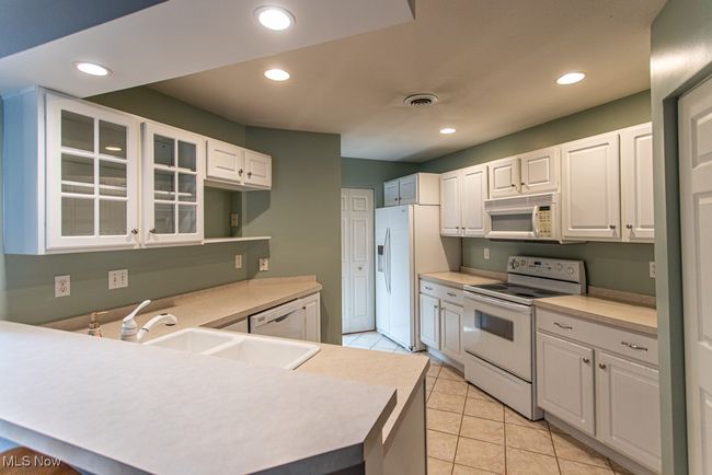 Kitchen featuring white appliances, recessed lighting, white cabinets, light tile patterned floors, and glass insert cabinets | Image 9