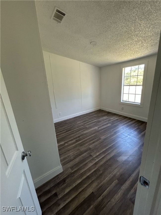 Empty room with baseboards, dark wood finished floors, and visible vents | Image 5