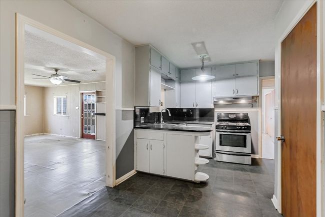 Kitchen with a textured ceiling, under cabinet range hood, a sink, stainless steel gas range, and dark countertops | Image 7