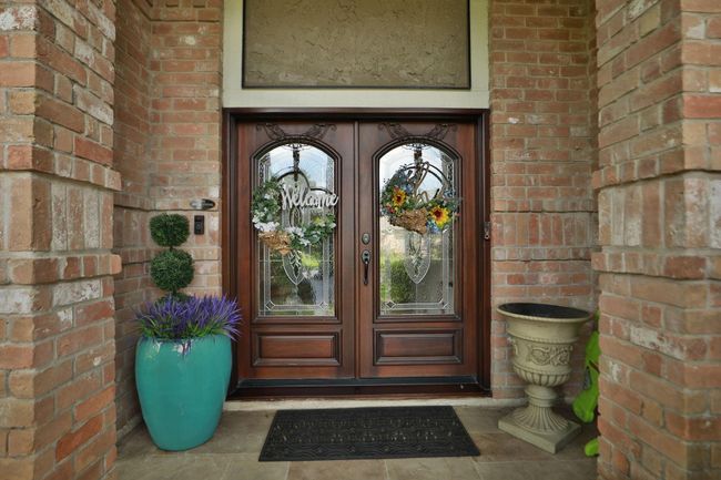 This charming residence features an inviting covered front entrance with decorative glass doors and an elegant brick exterior. | Image 4