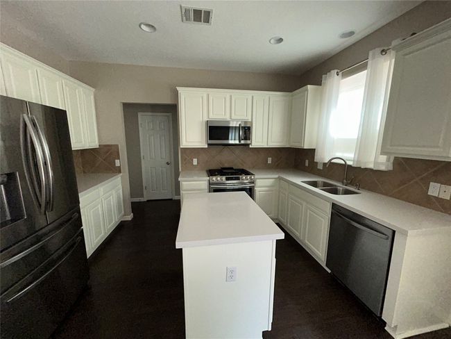 Kitchen featuring stainless steel appliances, a sink, a center island, white cabinetry, and tasteful backsplash | Image 12