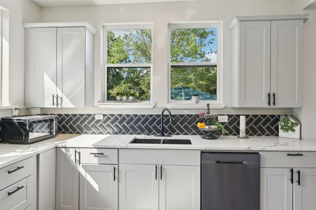 Kitchen featuring stainless steel dishwasher, a sink, decorative backsplash, white cabinetry, and light stone counters | Image 13