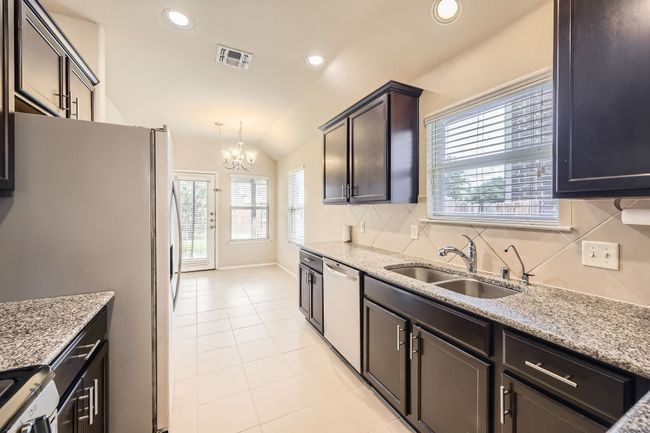 Kitchen with a chandelier, light stone countertops, light tile patterned flooring, dishwasher, and vaulted ceiling | Image 11