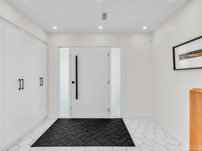 All newly renovated, gorgeous bright foyer with ultra modern front door, built in wall of brand new white cabinetry with black hardware, stunning honeycomb tiling, new staircase risers, treads and beautiful railing. | Image 7