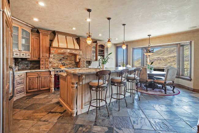 Kitchen featuring custom exhaust hood, high end stainless steel range, stone tile floors, and brown cabinets | Image 19