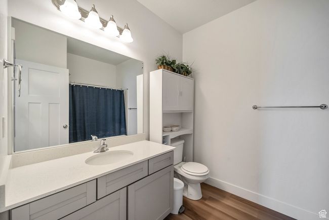 Full bath featuring a shower with curtain, toilet, baseboards, wood finished floors, and vanity | Image 10