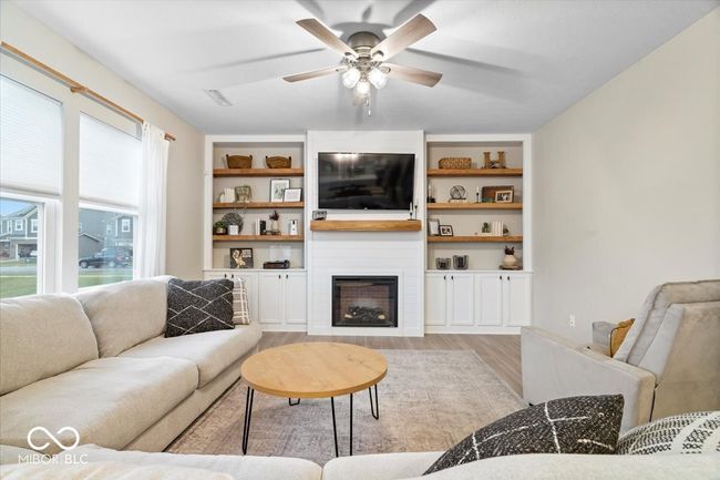 living room with light wood finished floors, a ceiling fan, a large fireplace, and built in features | Image 9