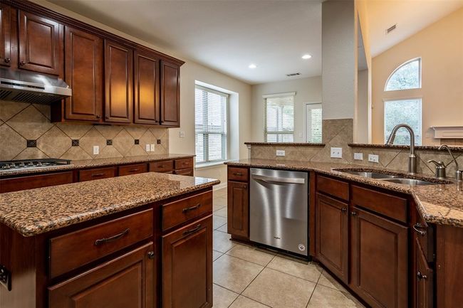 Kitchen with appliances with stainless steel finishes, under cabinet range hood, light tile patterned floors, dark stone counters, and decorative backsplash | Image 7