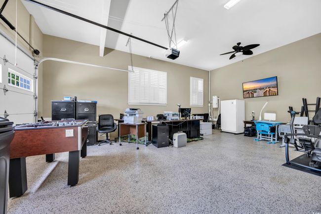 Rec room featuring speckle patterned floor, a desk, a ceiling fan, and a garage | Image 24