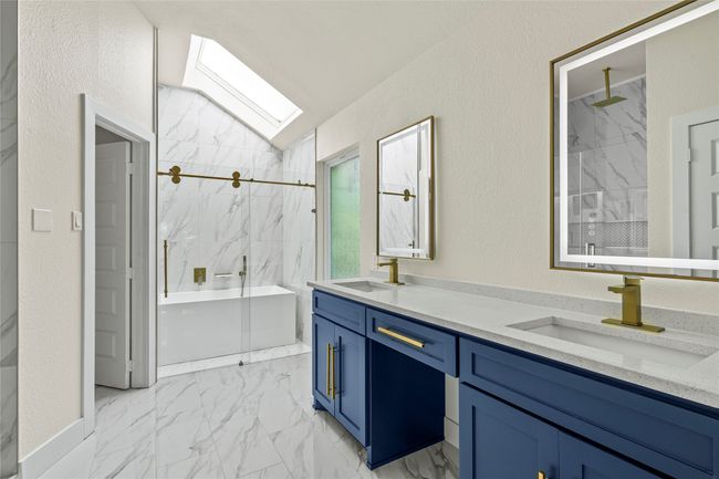 Bathroom featuring marble finish flooring, a marble finish shower, a bath, double vanity, and a skylight | Image 21