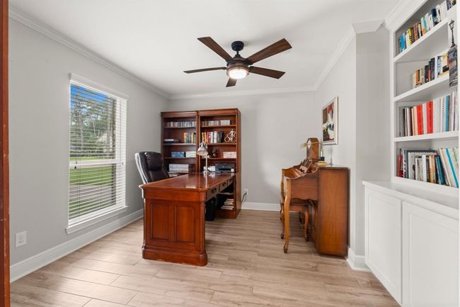 Home office featuring built-in bookshelves, and a large window. The room is well-lit with a ceiling fan offering a cozy and functional workspace. | Image 16