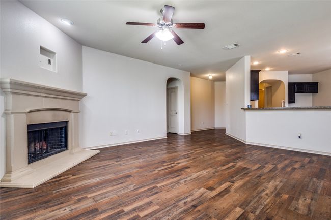 Unfurnished living room featuring arched walkways, ceiling fan, wood finished floors, a fireplace with raised hearth, and recessed lighting | Image 7