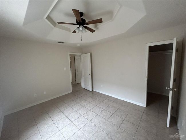 Unfurnished bedroom featuring a raised ceiling, a walk in closet, light tile patterned floors, and a ceiling fan | Image 8