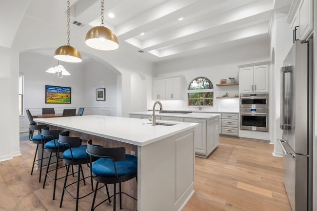 Kitchen featuring appliances with stainless steel finishes, an island with sink, arched walkways, a tray ceiling, and light wood finished floors | Image 8