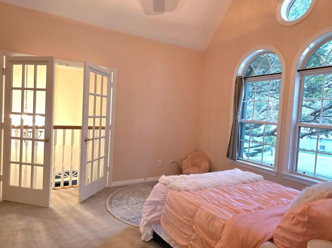 This cozy bedroom features a vaulted ceiling, soft peach walls, and ample natural light from large arched windows. French doors open to a hallway, adding elegance and charm. | Image 37