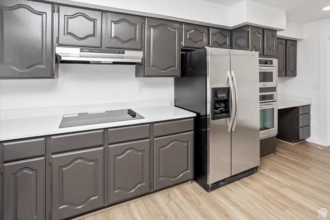 Kitchen with light countertops, gray cabinets, under cabinet range hood, light wood-style floors, and appliances with stainless steel finishes | Image 10