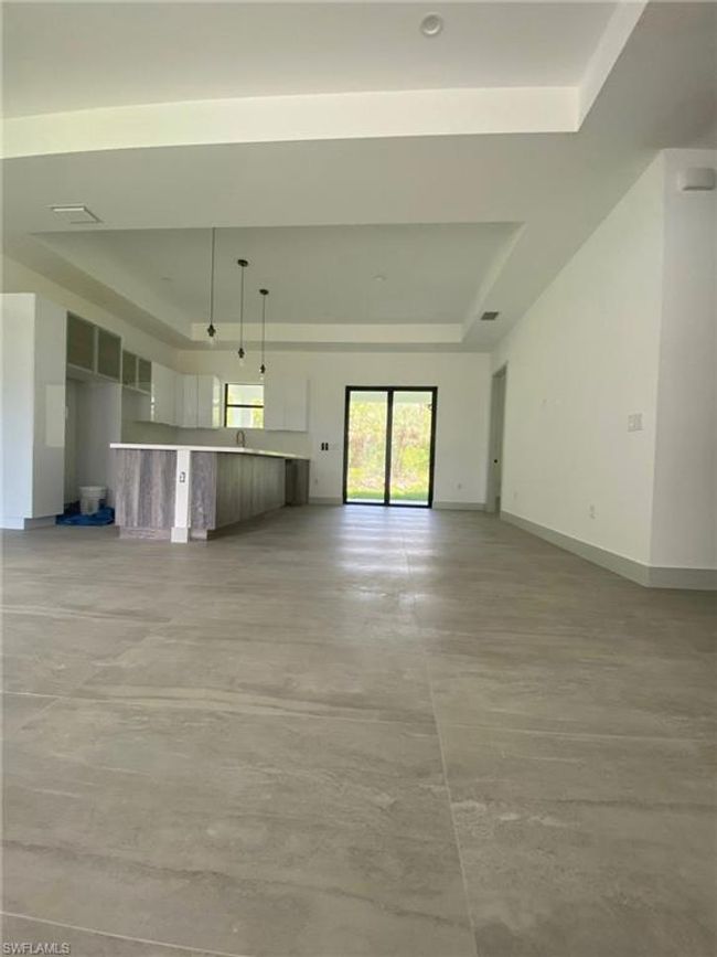 Unfurnished living room featuring concrete flooring, baseboards, and a tray ceiling | Image 6