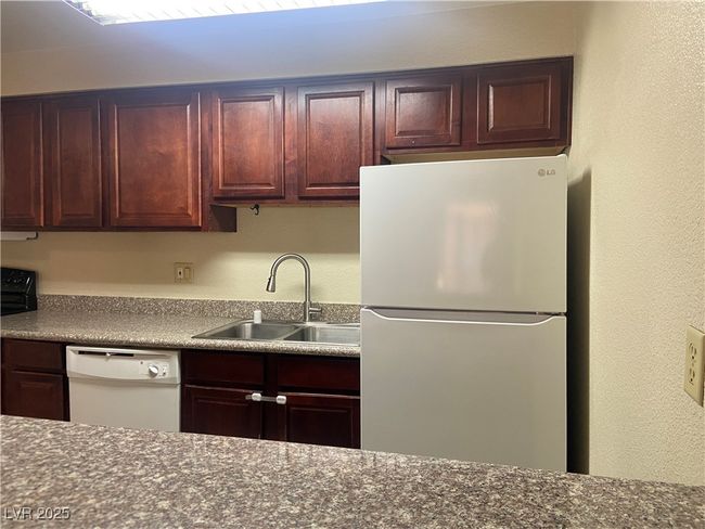 Kitchen with a sink, white appliances, dark countertops, and a textured wall | Image 9