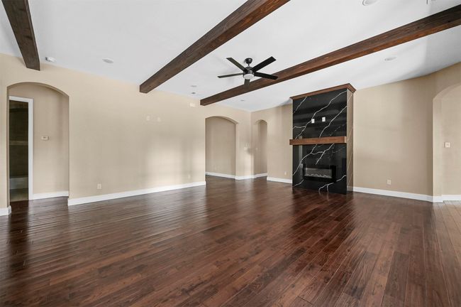 Unfurnished living room featuring arched walkways, dark wood-style flooring, beamed ceiling, and a high end fireplace | Image 21