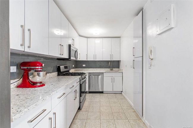 Kitchen featuring light stone counters, appliances with stainless steel finishes, backsplash, a sink, and white cabinetry | Image 7