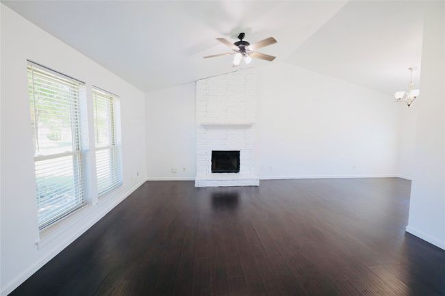 living room featuring vaulted ceiling, dark wood finished floors, a large fireplace, a chandelier, and a ceiling fan | Image 7