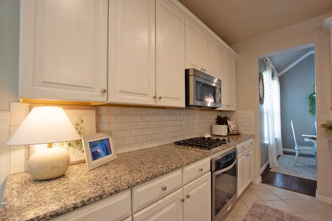 Kitchen featuring light stone counters, stainless steel appliances, white cabinetry, light tile patterned floors, and tasteful backsplash | Image 11