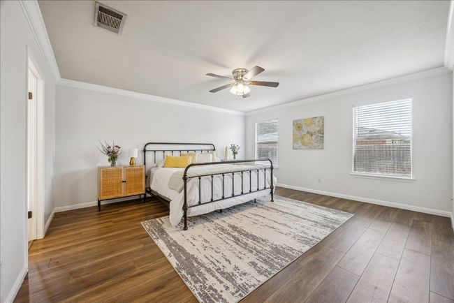 Primary bedroom featuring crown molding, vinyl flooring, large windows allowing natural light from the yard, and a ceiling fan | Image 13