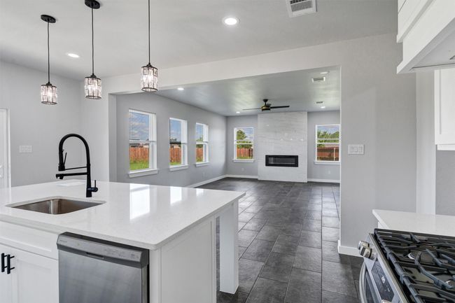 Kitchen featuring stainless steel appliances, a sink, baseboards, ceiling fan, and a tile fireplace | Image 17