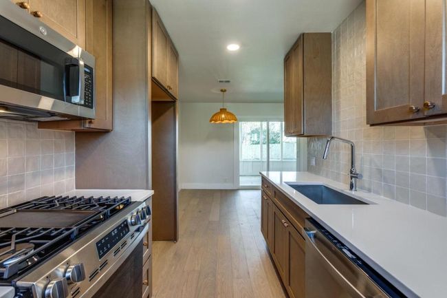 Kitchen featuring a sink, light countertops, appliances with stainless steel finishes, backsplash, and light wood finished floors | Image 5
