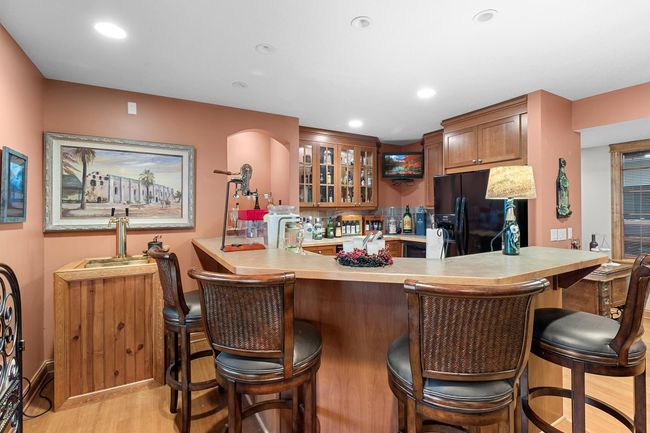 Lower-level recreation room wet bar. Cherry cabinets, sink, garbage disposal, dishwasher, full-sized refrigerator, separate wine refrigerator, microwave, TV included in listing | Image 44