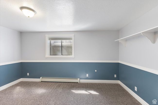 Carpeted empty room with a baseboard radiator, baseboards, and a textured ceiling | Image 23