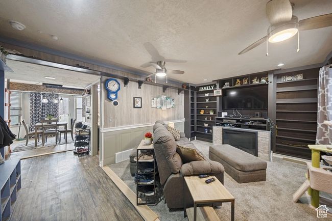 Living area featuring a textured ceiling, a decorative wall, wood finished floors, a ceiling fan, and a glass covered fireplace | Image 4