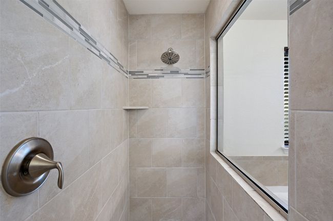 Primary bathroom features a modern walk-in shower with clean, contemporary tile and a window overlooking the soaking tub. | Image 23