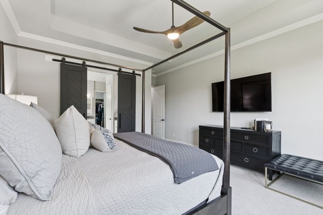 Carpeted bedroom featuring a barn door, ornamental molding, a ceiling fan, and a raised ceiling | Image 18