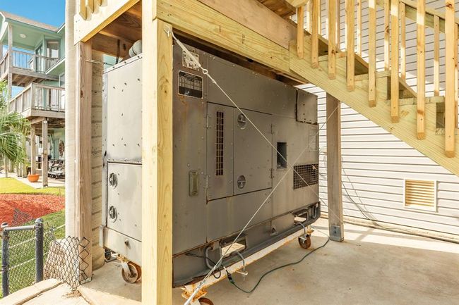 This photo shows an outdoor area with a large commercial generator set under a recently installed wooden staircase. The space is covered and part of a home with nearby siding and a fenced yard, suggesting additional utility and emergency power capabilities. | Image 41
