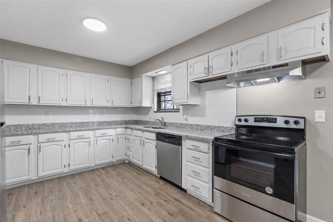 Kitchen with light wood-type flooring, white cabinets, under cabinet range hood, and appliances with stainless steel finishes | Image 9