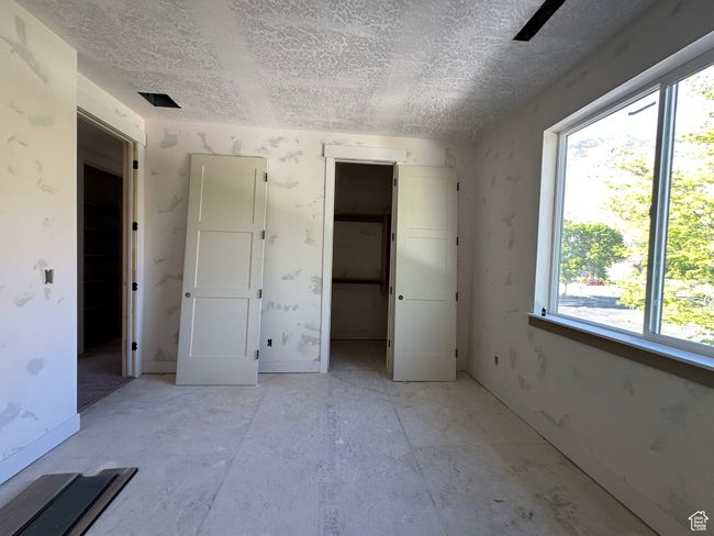 Unfurnished bedroom with a textured ceiling, multiple windows, a walk in closet, and a closet | Image 17