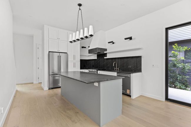 Kitchen with stainless steel appliances, wall chimney range hood, light wood-style flooring, and tasteful backsplash | Image 11