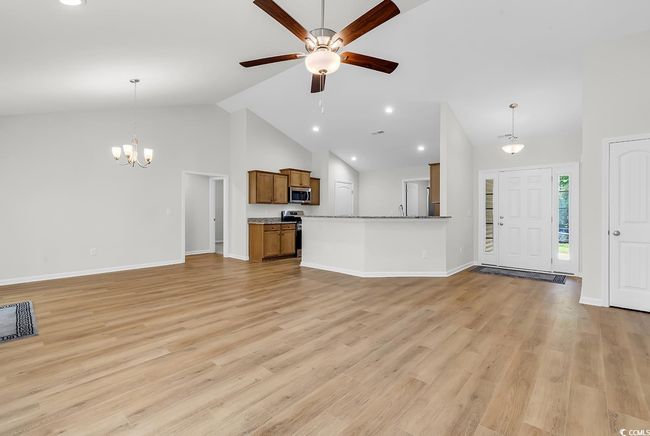 Unfurnished living room with high vaulted ceiling, a ceiling fan, a chandelier, baseboards, and light wood-style floors | Image 7
