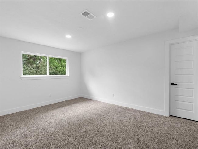 This is a bright, spacious room with neutral walls and carpeted flooring. It features a large window providing natural light and a modern white door. Ideal for a bedroom or home office. | Image 30