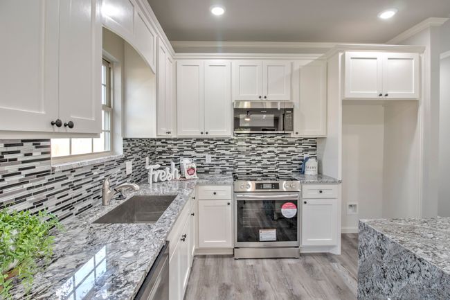 Kitchen featuring appliances with stainless steel finishes, white cabinetry, crown molding, decorative backsplash, and light stone countertops | Image 9
