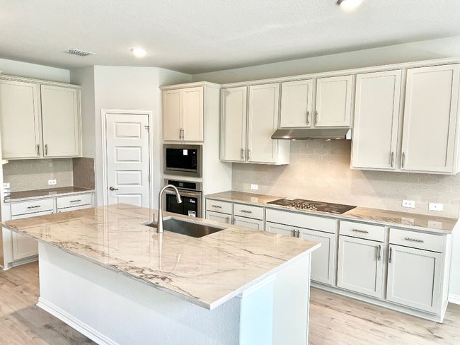 Kitchen with backsplash, light stone counters, light wood-type flooring, a kitchen island with sink, and recessed lighting | Image 7