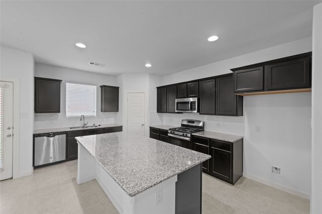 Kitchen featuring appliances with stainless steel finishes, a kitchen island, light stone counters, dark cabinets, and recessed lighting | Image 12